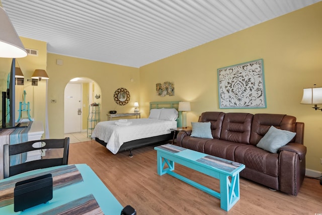 bedroom featuring light wood-type flooring, arched walkways, and visible vents