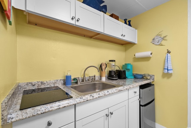 kitchen with light stone counters, black electric stovetop, a sink, and white cabinetry