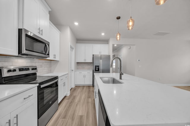 kitchen with backsplash, a kitchen island with sink, stainless steel appliances, light wood-style floors, and a sink