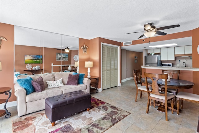 living area featuring light tile patterned floors, a ceiling fan, baseboards, visible vents, and a textured ceiling