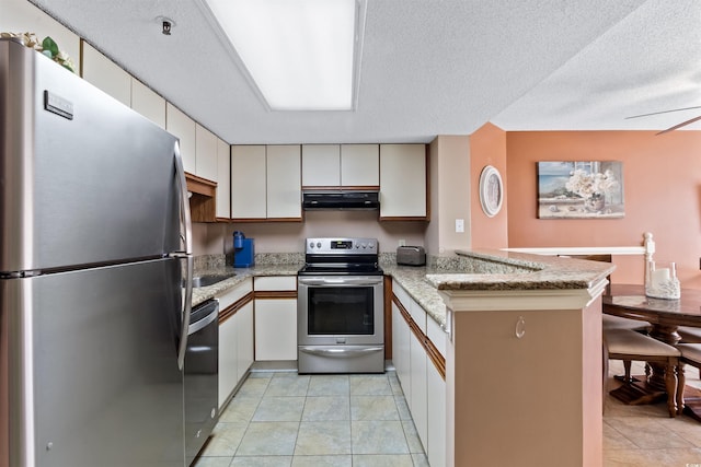 kitchen with under cabinet range hood, appliances with stainless steel finishes, a peninsula, and light tile patterned flooring