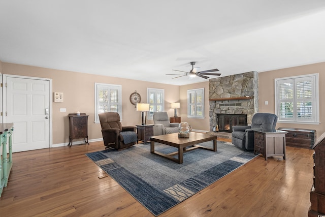 living area featuring a ceiling fan, a fireplace, baseboards, and wood finished floors