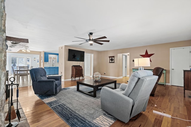 living area with wood finished floors, a ceiling fan, and baseboards