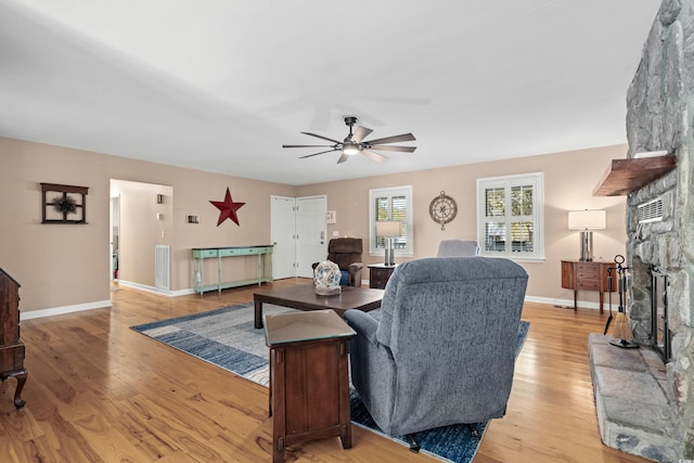 living area with light wood-type flooring, visible vents, baseboards, and a stone fireplace