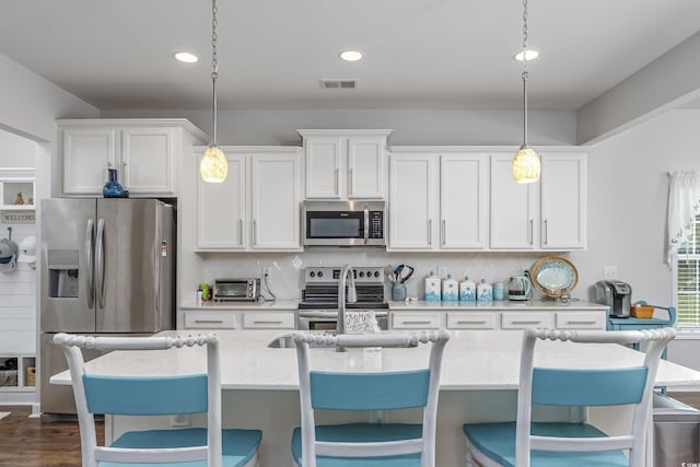 kitchen with visible vents, decorative light fixtures, stainless steel appliances, white cabinetry, and backsplash