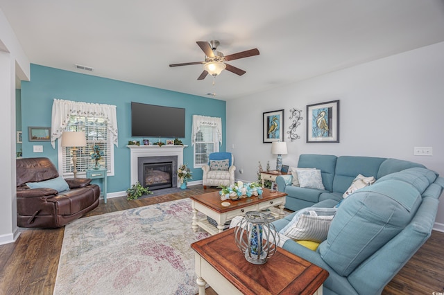 living room featuring visible vents, baseboards, dark wood-style floors, ceiling fan, and a fireplace with flush hearth