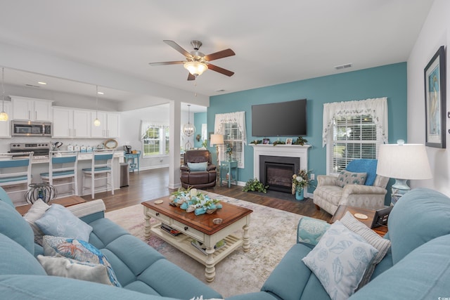 living room with a fireplace with flush hearth, visible vents, a ceiling fan, baseboards, and dark wood-style floors