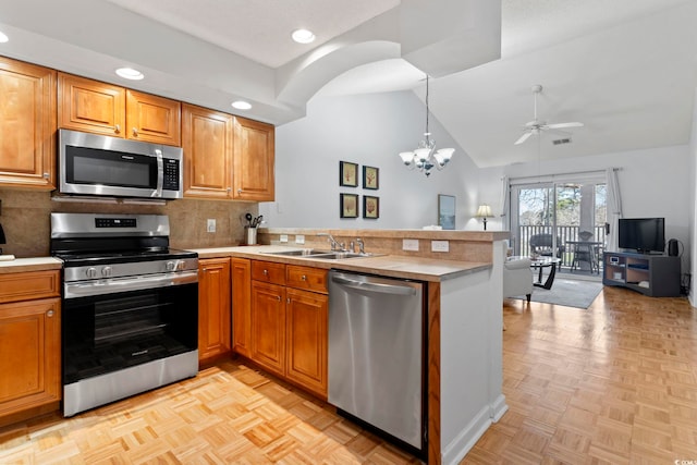 kitchen featuring appliances with stainless steel finishes, a peninsula, vaulted ceiling, light countertops, and a sink