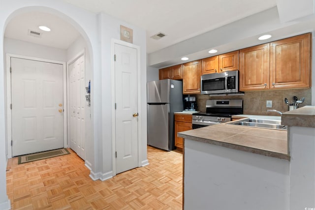 kitchen featuring arched walkways, visible vents, appliances with stainless steel finishes, brown cabinetry, and a sink