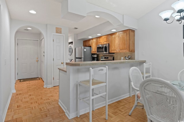 kitchen featuring arched walkways, stainless steel appliances, a breakfast bar, and stacked washing maching and dryer