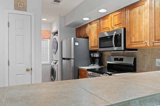 kitchen featuring stacked washer / dryer, visible vents, light countertops, appliances with stainless steel finishes, and backsplash