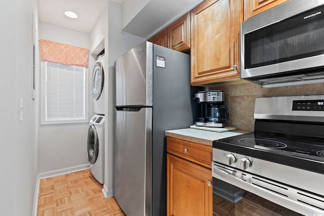 kitchen with baseboards, stacked washer / drying machine, stainless steel appliances, light countertops, and backsplash