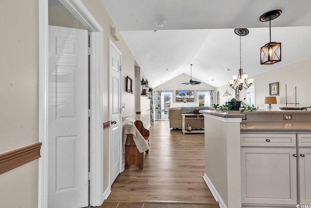 corridor with light wood-style floors, a chandelier, and vaulted ceiling