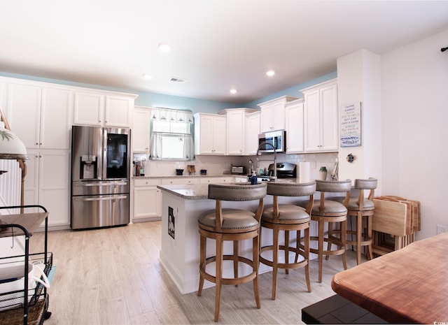 kitchen featuring stainless steel appliances, backsplash, light wood-style floors, white cabinets, and a kitchen breakfast bar