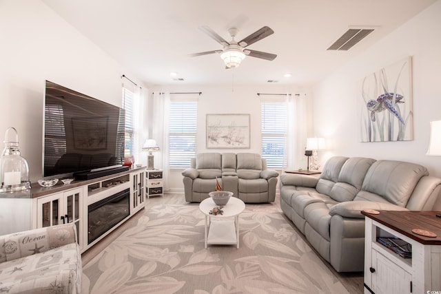 living room with a glass covered fireplace, visible vents, and a ceiling fan