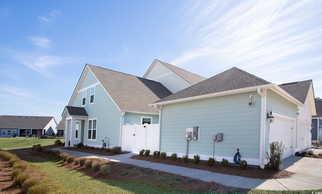 view of property exterior featuring roof with shingles, a lawn, and an attached garage