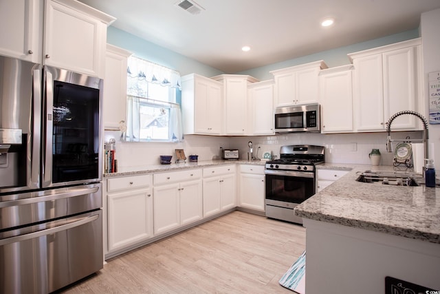 kitchen with appliances with stainless steel finishes, visible vents, a sink, and light stone counters