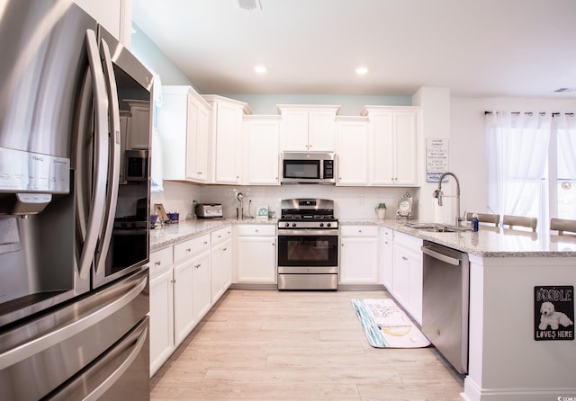 kitchen with light stone counters, appliances with stainless steel finishes, white cabinets, and a sink