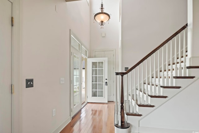 foyer entrance featuring stairs, a high ceiling, baseboards, and light wood-style floors