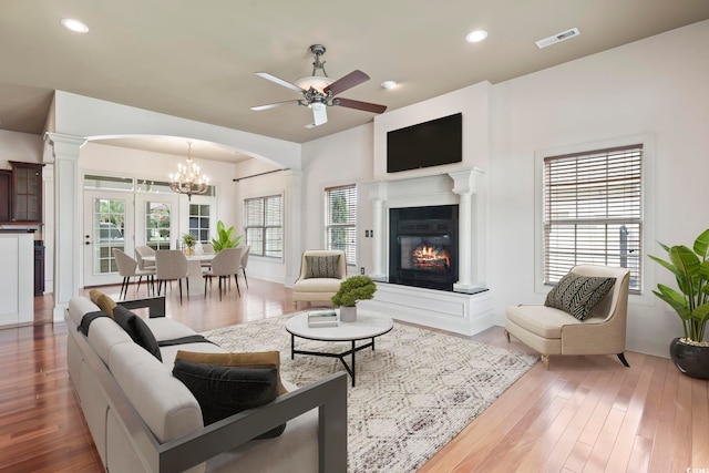 living area with decorative columns, arched walkways, wood finished floors, and a glass covered fireplace