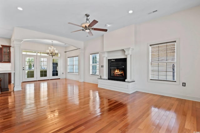 unfurnished living room with ceiling fan with notable chandelier, light wood-type flooring, a glass covered fireplace, and visible vents