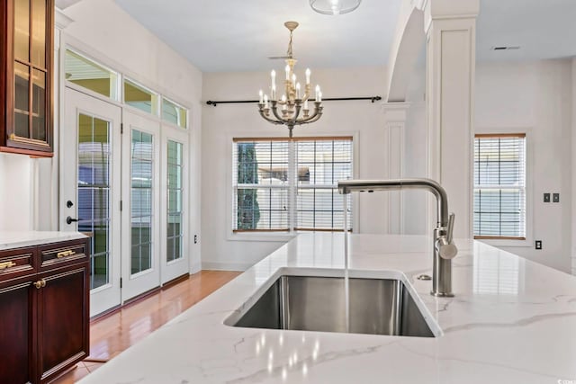 kitchen with pendant lighting, a notable chandelier, glass insert cabinets, a sink, and light stone countertops