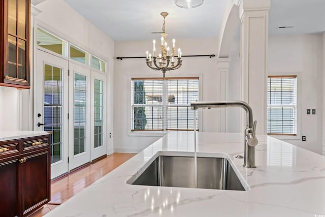 kitchen featuring a sink, plenty of natural light, light stone countertops, decorative light fixtures, and a chandelier