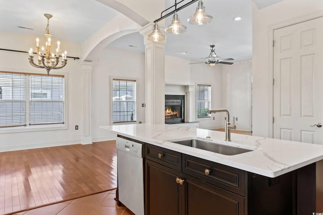 kitchen featuring a warm lit fireplace, dishwasher, a sink, ceiling fan with notable chandelier, and open floor plan