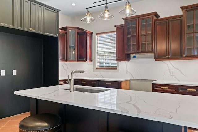 kitchen featuring a sink, light stone counters, decorative backsplash, glass insert cabinets, and hanging light fixtures