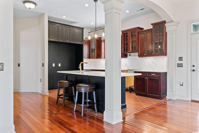 kitchen featuring decorative light fixtures, visible vents, light countertops, tasteful backsplash, and glass insert cabinets