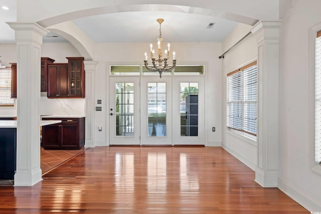 doorway featuring a notable chandelier, wood finished floors, visible vents, baseboards, and decorative columns