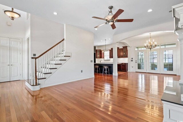 unfurnished living room featuring light wood-type flooring, decorative columns, and ceiling fan with notable chandelier