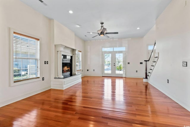 unfurnished living room featuring french doors, light wood-type flooring, a glass covered fireplace, and a wealth of natural light