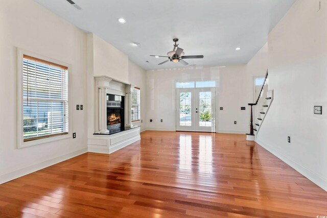 unfurnished living room featuring french doors, stairway, ceiling fan, a glass covered fireplace, and light wood-style floors