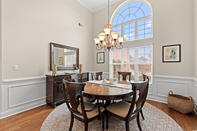 dining space featuring a wainscoted wall, visible vents, ornamental molding, wood finished floors, and a chandelier