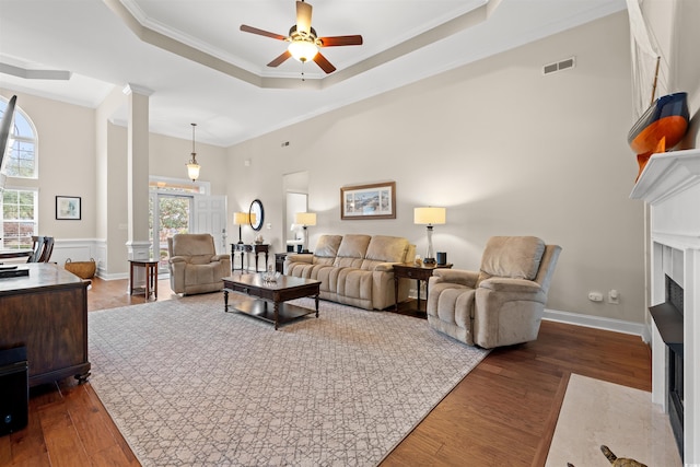 living area with plenty of natural light, visible vents, a fireplace with flush hearth, wood finished floors, and a tray ceiling