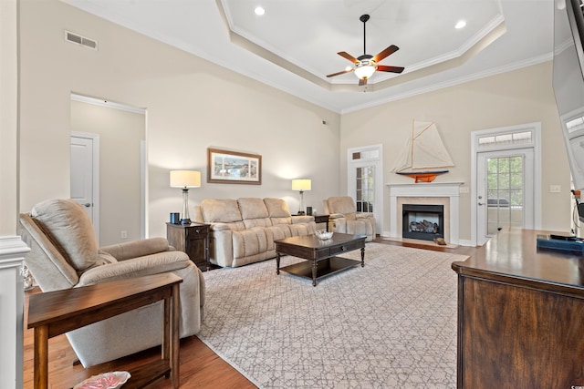 living area with a fireplace with flush hearth, wood finished floors, visible vents, ornamental molding, and a tray ceiling