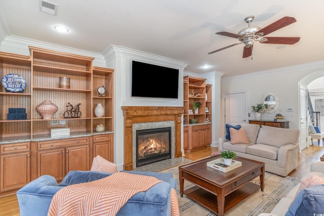 living room with visible vents, arched walkways, ceiling fan, ornamental molding, and a fireplace