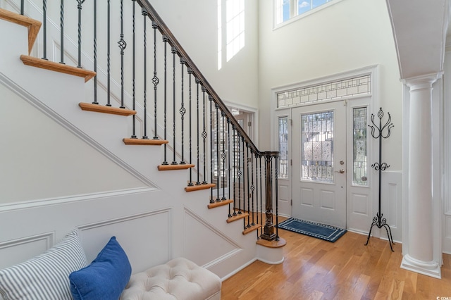 entrance foyer with decorative columns, a high ceiling, and light wood-style flooring