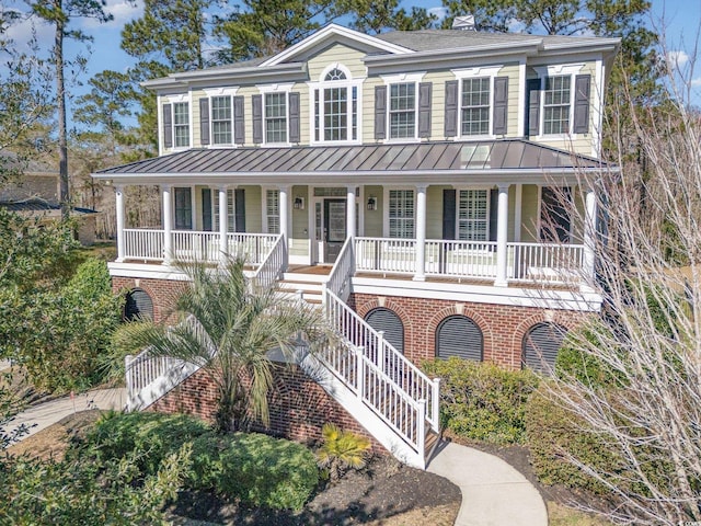 view of front of home with stairs, brick siding, a standing seam roof, and covered porch