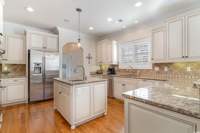 kitchen with arched walkways, decorative light fixtures, stainless steel appliances, a sink, and a center island with sink