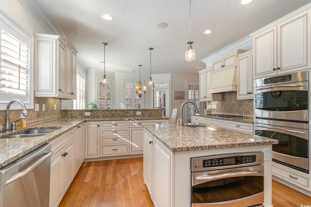 kitchen with stainless steel appliances, pendant lighting, a kitchen island with sink, and a sink