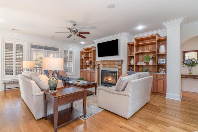 living area featuring crown molding, visible vents, light wood-style flooring, a glass covered fireplace, and ceiling fan