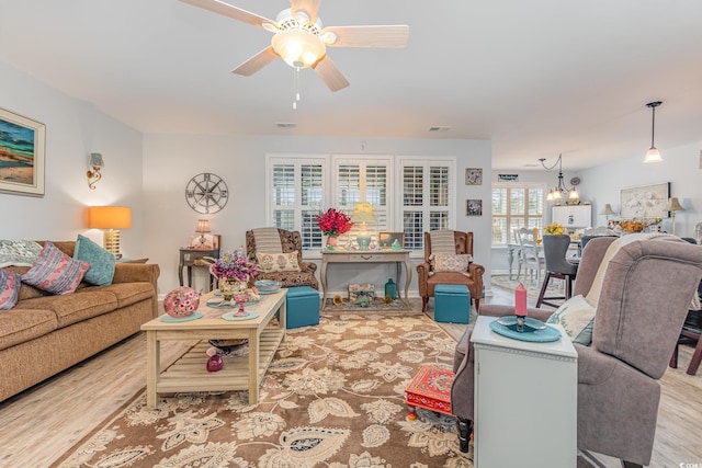 living room featuring ceiling fan with notable chandelier, visible vents, and wood finished floors