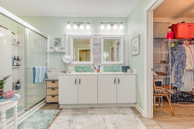 bathroom featuring double vanity, wood finished floors, a stall shower, and a sink