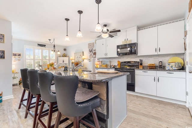 kitchen with tasteful backsplash, a breakfast bar, light wood-style floors, and black appliances