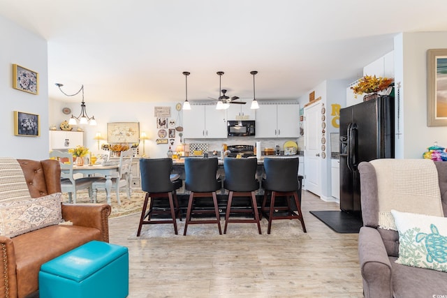 interior space with tasteful backsplash, open floor plan, light wood finished floors, and black appliances