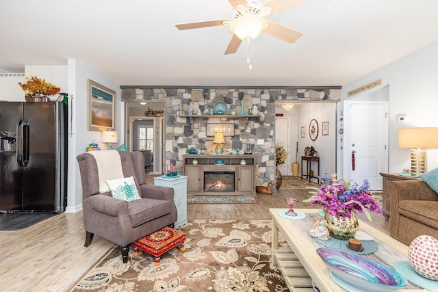 living room featuring ceiling fan, wood finished floors, and a stone fireplace