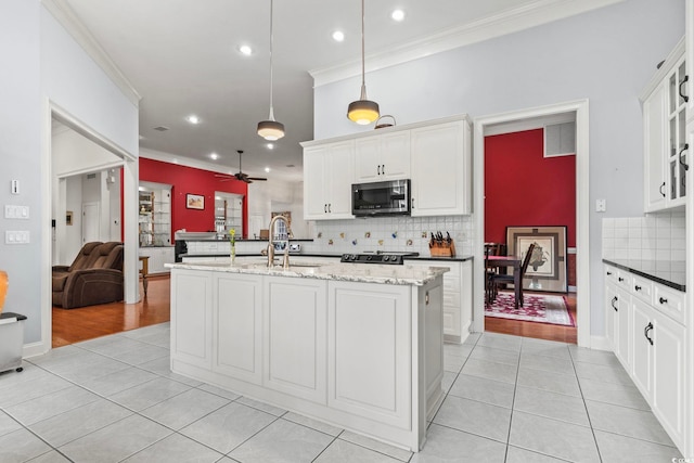 kitchen featuring light tile patterned floors, a sink, open floor plan, ornamental molding, and stainless steel microwave