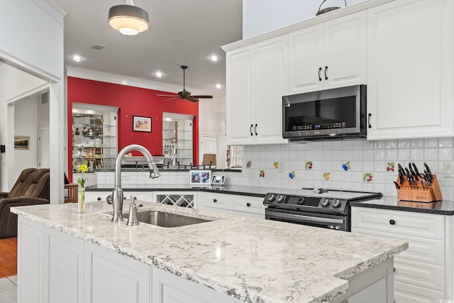 kitchen with stainless steel microwave, backsplash, a sink, light stone countertops, and range with electric cooktop